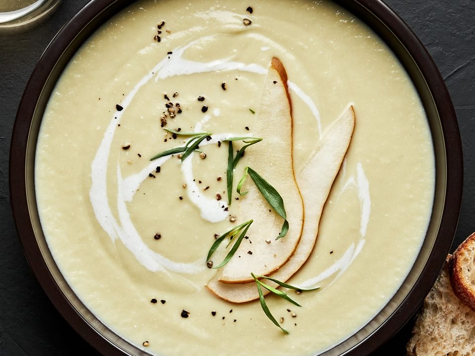 a bowl of pear and buttermilk bisque sprinkled with salt, pepper & tarragon with a pear slice garnish on top