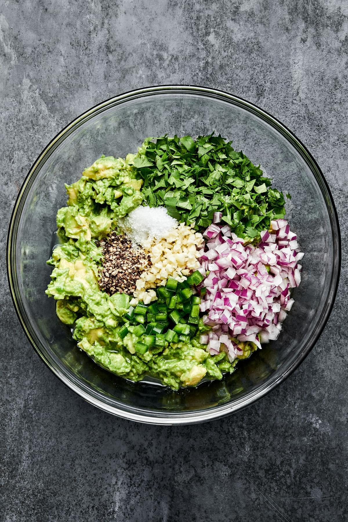 avocados, garlic, pepper, cilantro, jalapeño, red onion, limes and salt in a glass bowl
