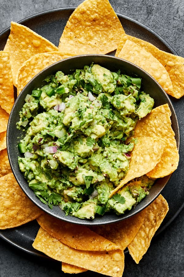 a bowl of homemade guacamole with red onion, jalapeño and cilantro surrounded by tortilla chips