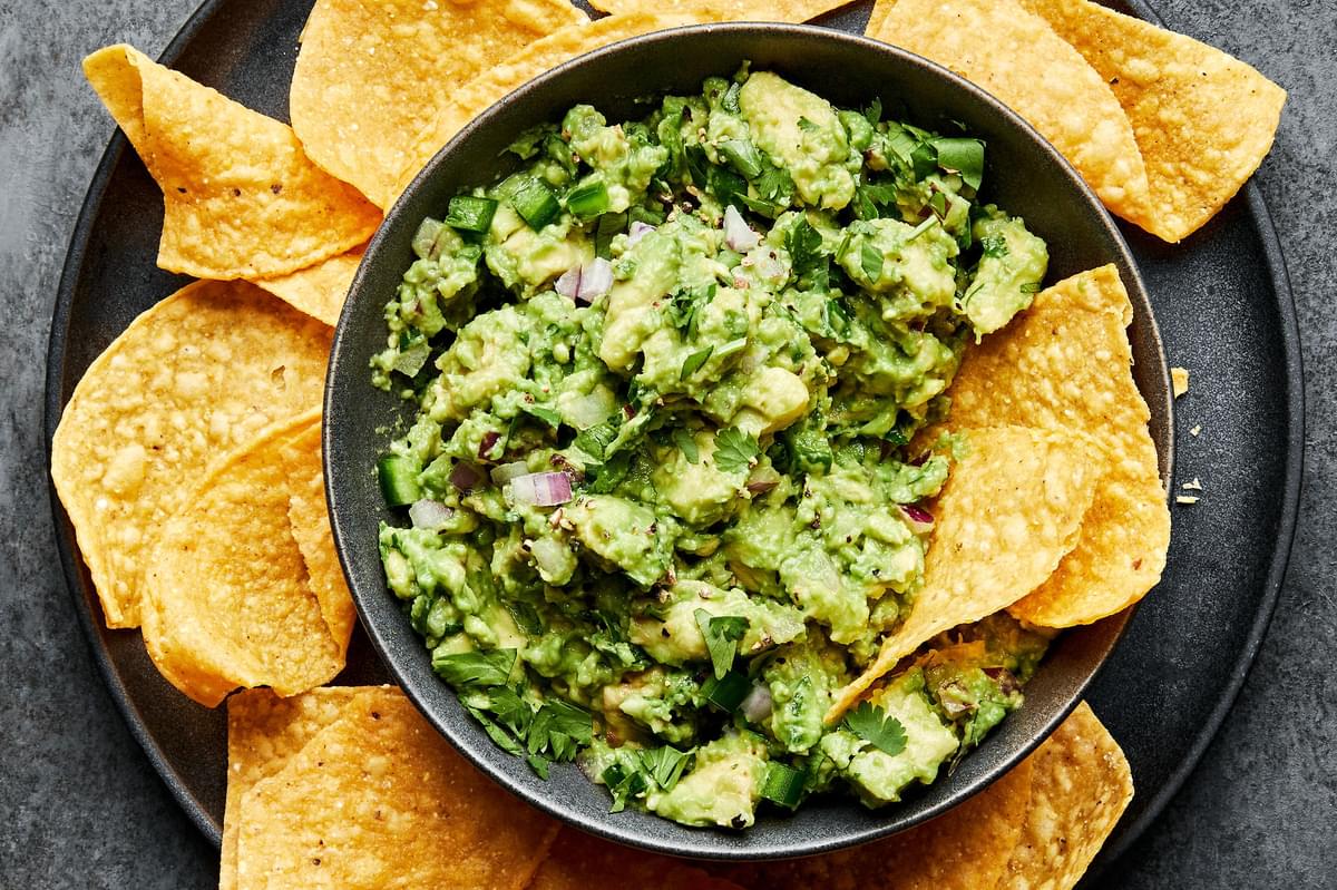 a bowl of homemade guacamole with red onion, jalapeño and cilantro surrounded by tortilla chips