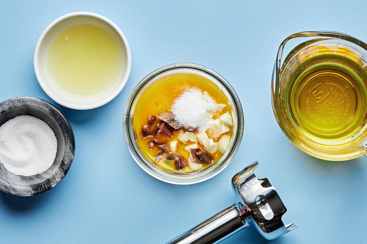 egg yolks, anchovies, garlic, salt, and lemon juice in a glass jar next to an immersion blender to make pesto Caesar dressing