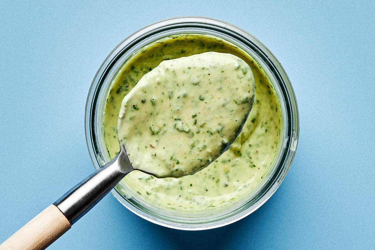 homemade pesto Caesar salad dressing being scooped out of a glass jar