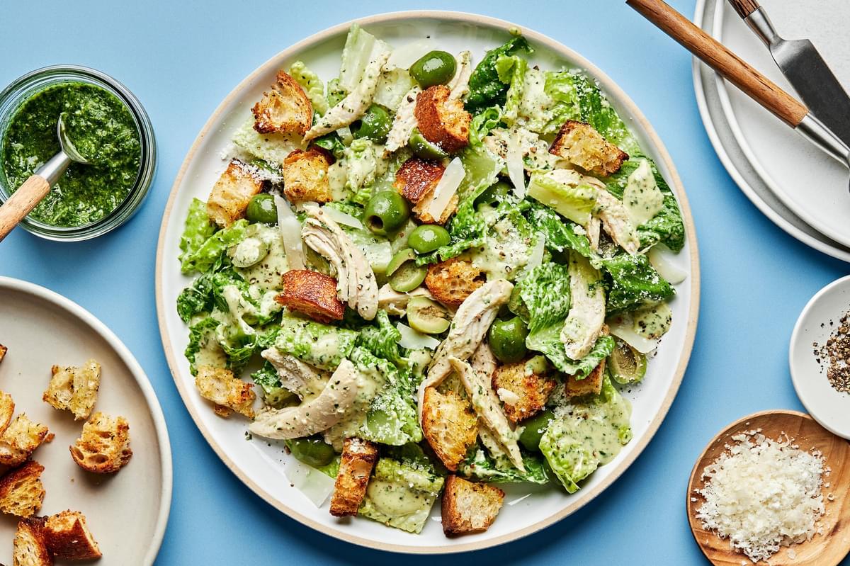Pesto Caesar Salad with castelvetrano Olives, shredded chicken, parmesan and homemade croutons on a plate