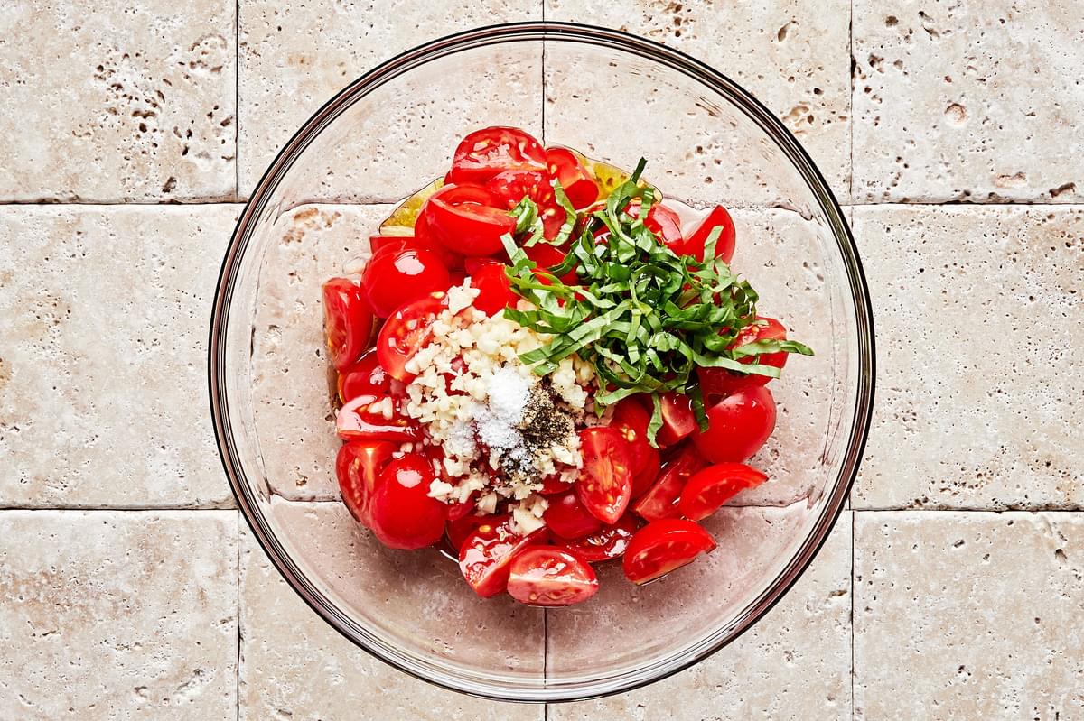 halved cherry tomatoes, garlic, salt, pepper, olive oil, vinegar, lemon juice, and basil in a glass bowl