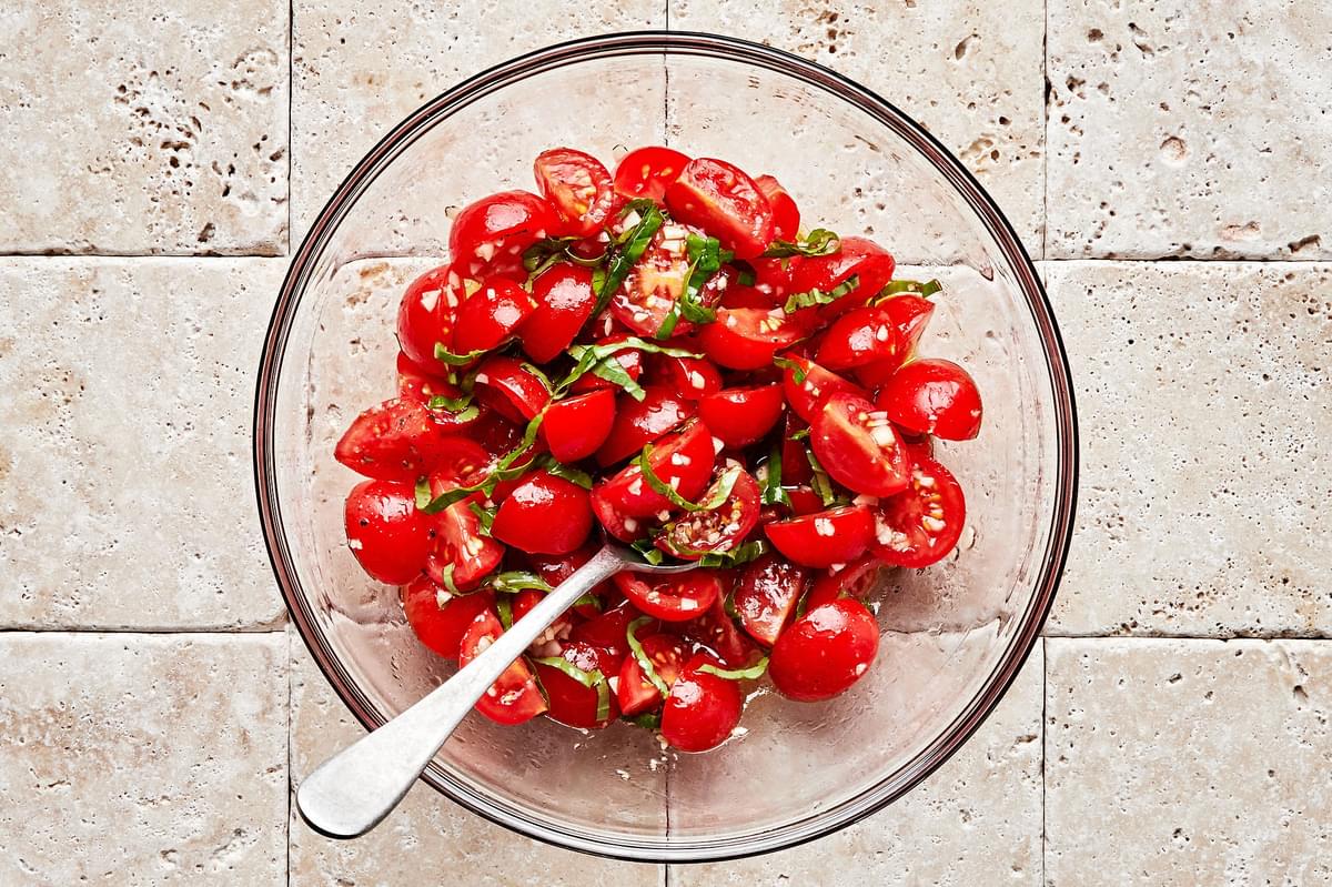 bruschetta in a glass bowl made with cherry tomatoes, garlic, salt, pepper, olive oil, vinegar, lemon juice, and basil