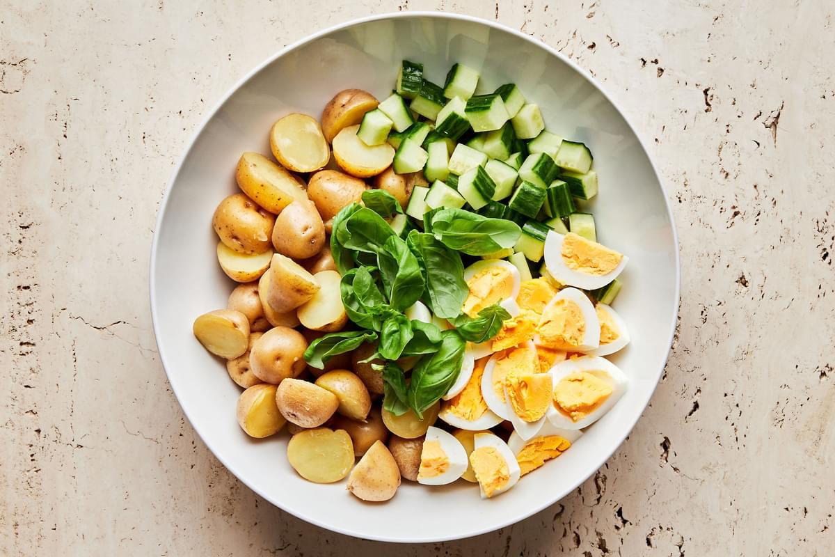 boiled potatoes, boiled eggs, cucumbers and fresh basil in a large serving bowl