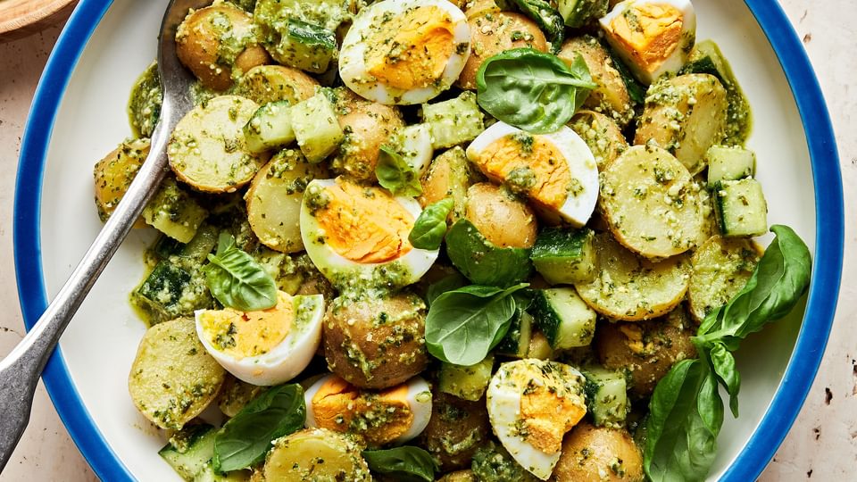 pesto potato salad in a serving bowl made with potatoes, eggs, cucumbers and fresh basil