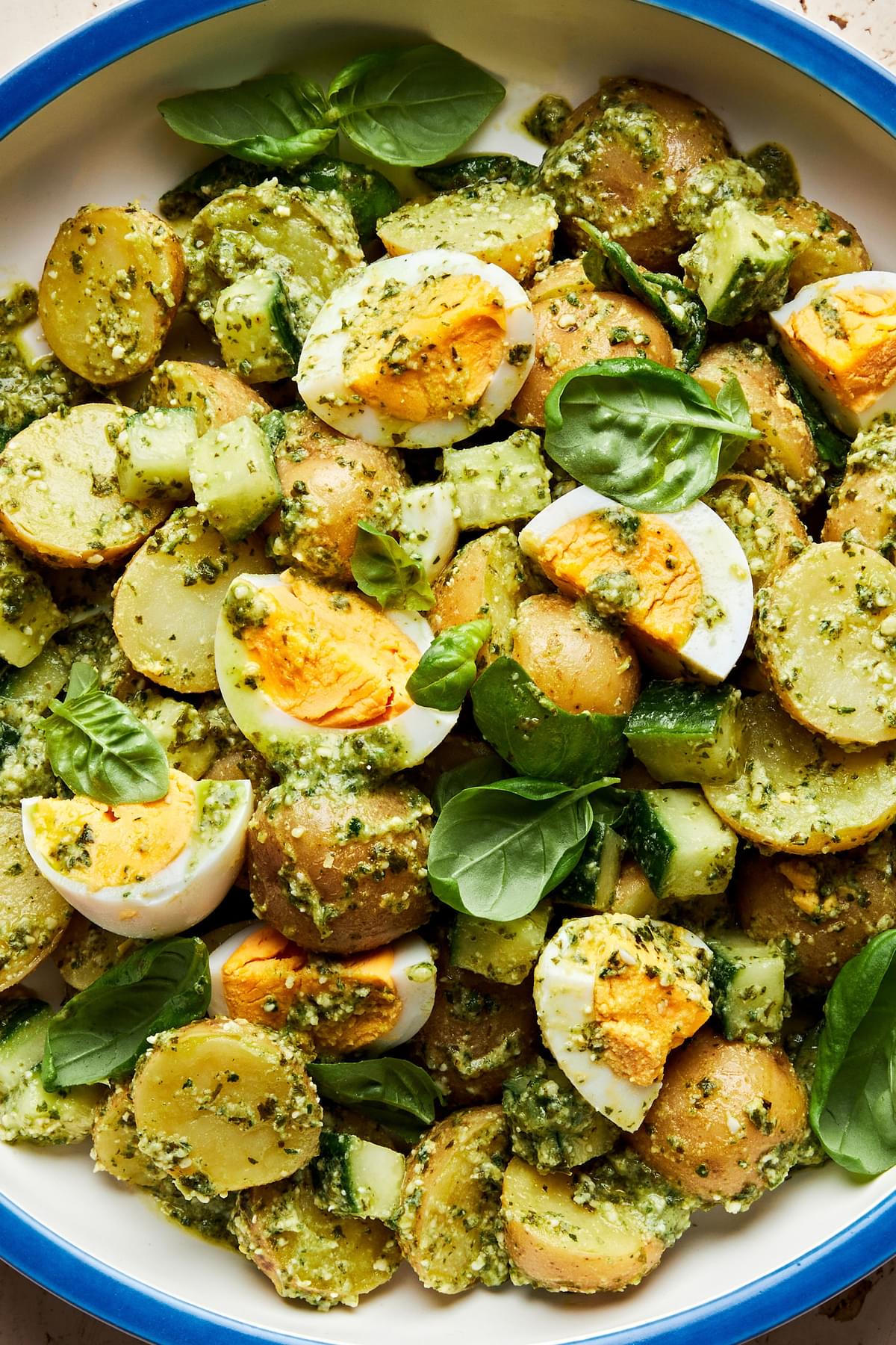 pesto potato salad in a serving bowl made with potatoes, eggs, cucumbers and fresh basil
