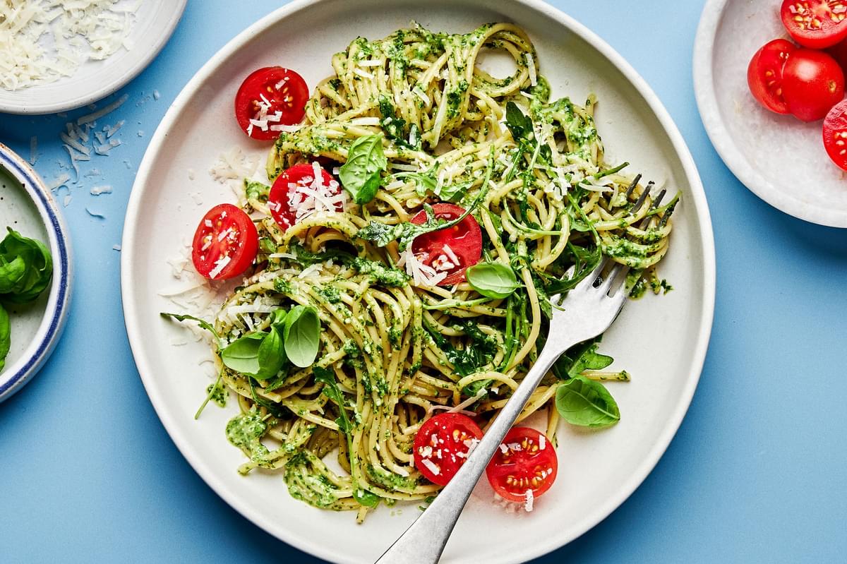 a plate of homemade pesto spaghetti with arugula and cherry tomatoes and sprinkled with basil and parmesan