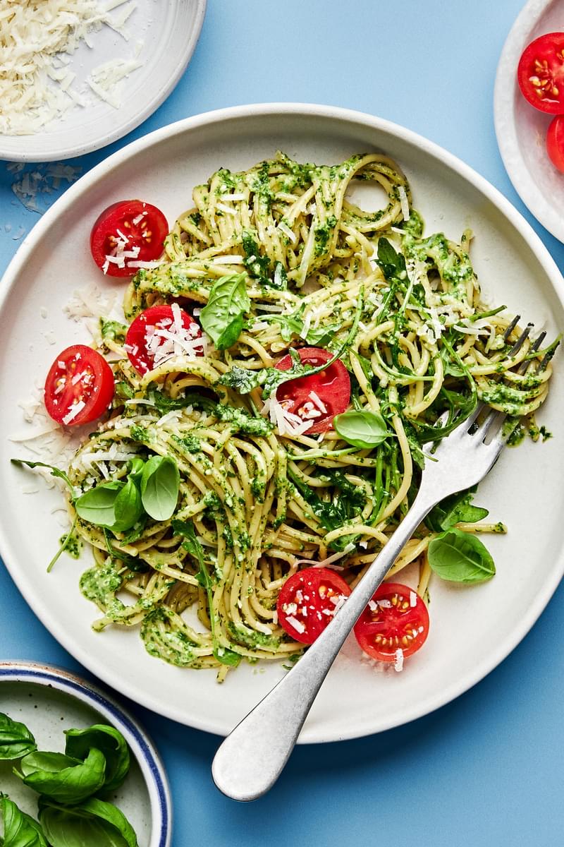 a plate of homemade pesto spaghetti with arugula and cherry tomatoes and sprinkled with basil and parmesan