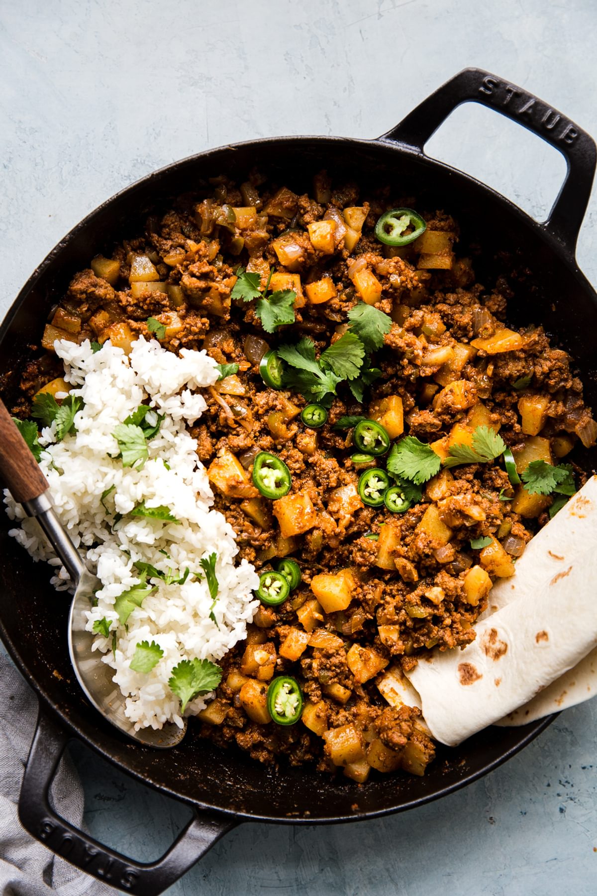 Mexican picadillo in a skillet with ground beef, potatoes, onion, cumin, tomato paste and spices. Served with rice