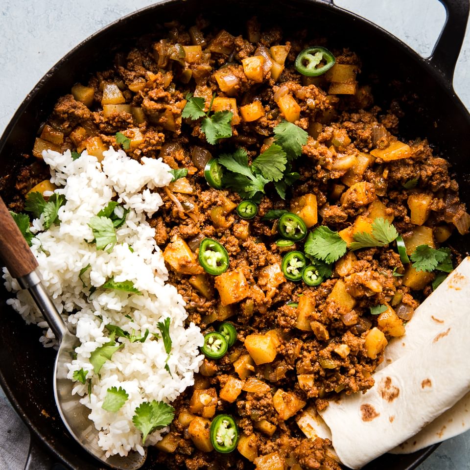 Mexican picadillo in a skillet with ground beef, potatoes, onion, cumin, tomato paste and spices. Served with rice