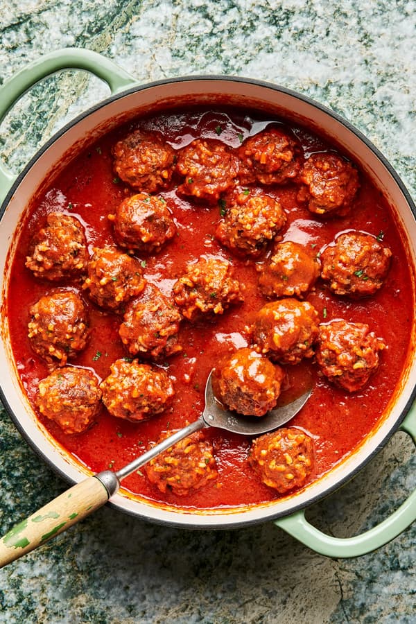 a skillet filled with homemade porcupine meatballs in tomato sauce with a serving spoon.