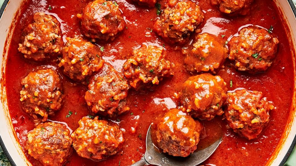 a skillet filled with homemade porcupine meatballs in tomato sauce with a serving spoon.
