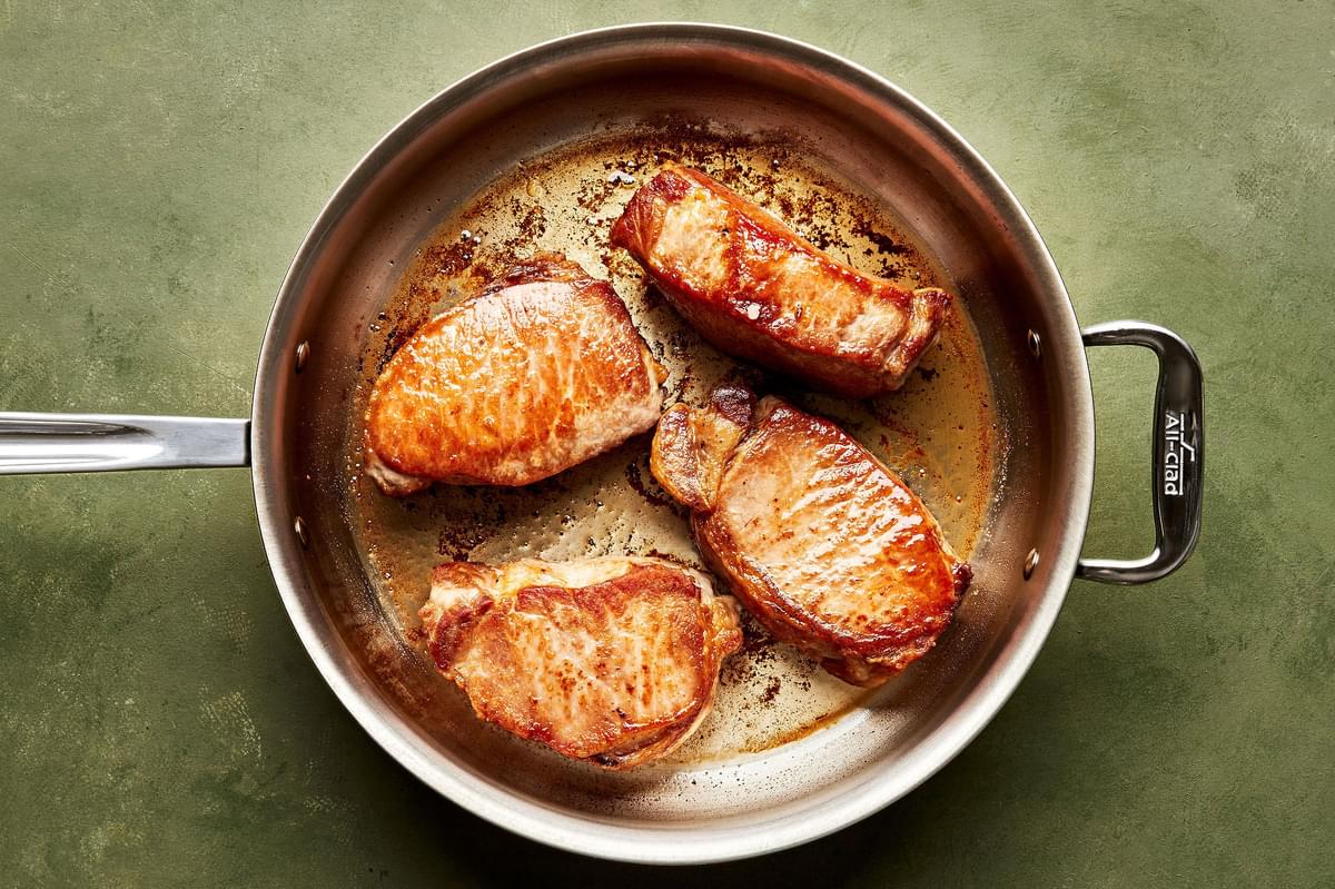 pork chops seasoned with salt being seared in a skillet with olive oil