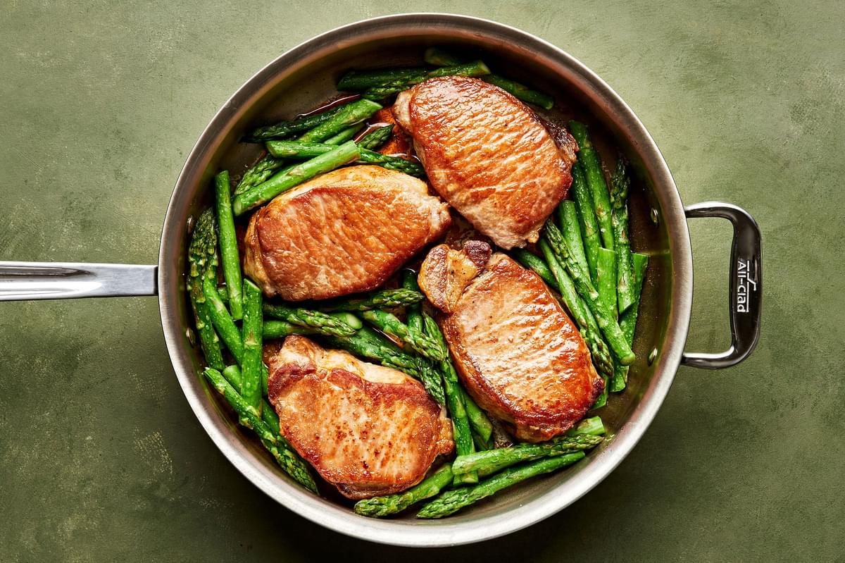 seared pork chops and asparagus in a skillet