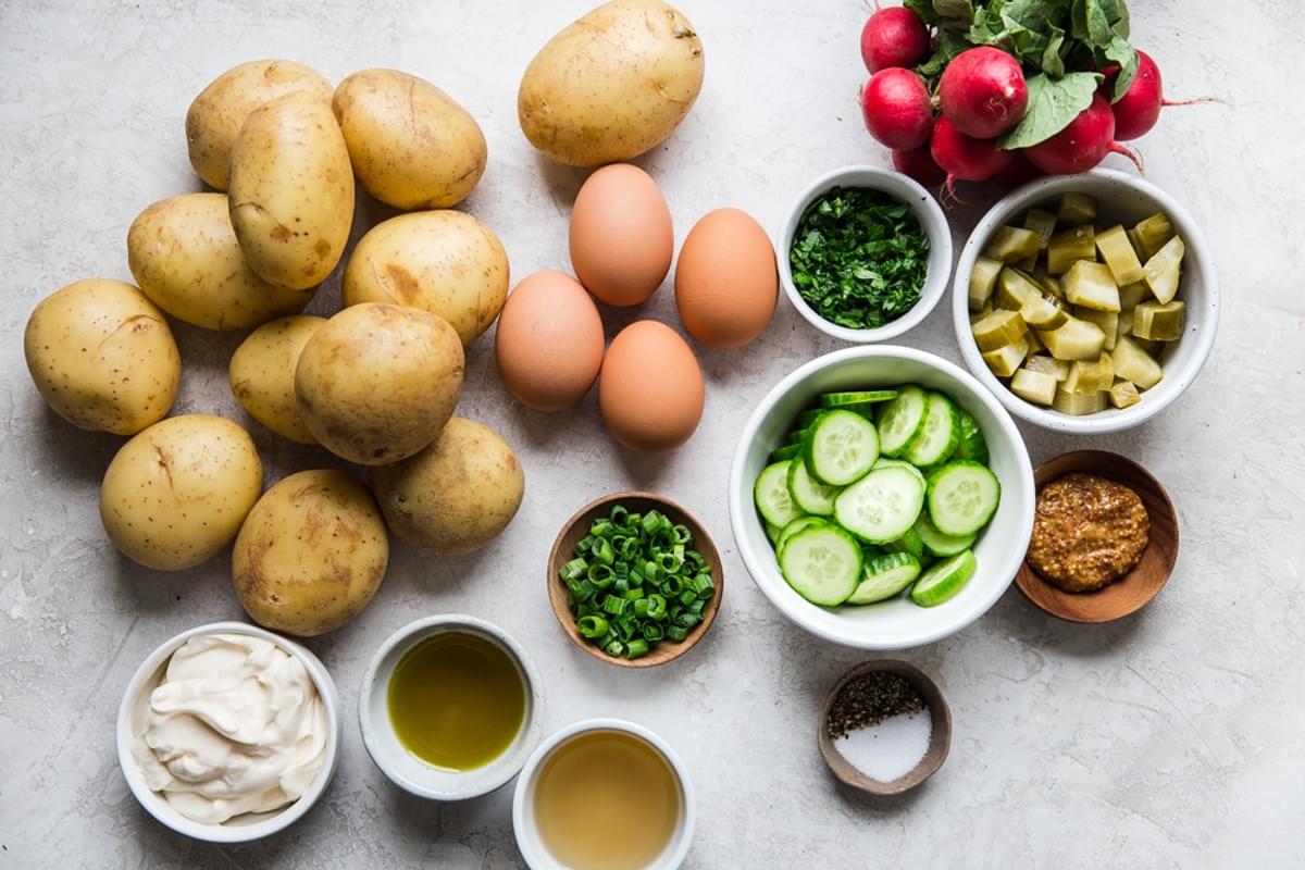 Ingredients laid out for potato salad hard boiled eggs, cucumbers, pickles, radishes olive oil vinegar mayonnaise