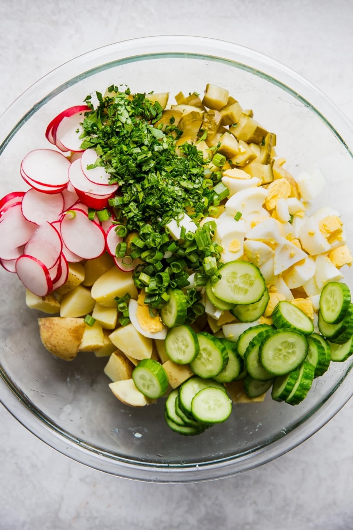 Ingredients in a bowl for potato salad hard boiled eggs, cucumbers, pickles, radishes olive oil vinegar mayonnaise