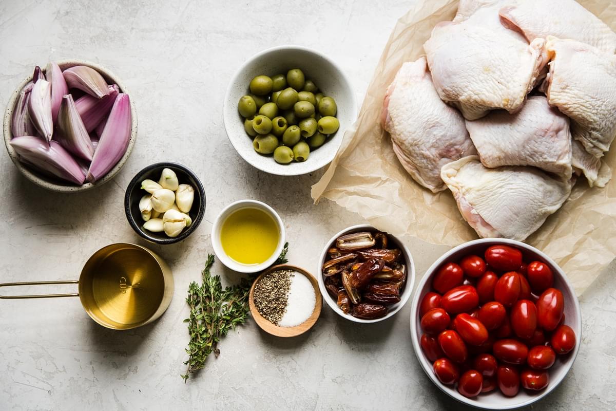 Ingredients laid out for chicken Provençal tomatoes, green olives, bone in skin on chicken thighs, olive oil, dates, shallots