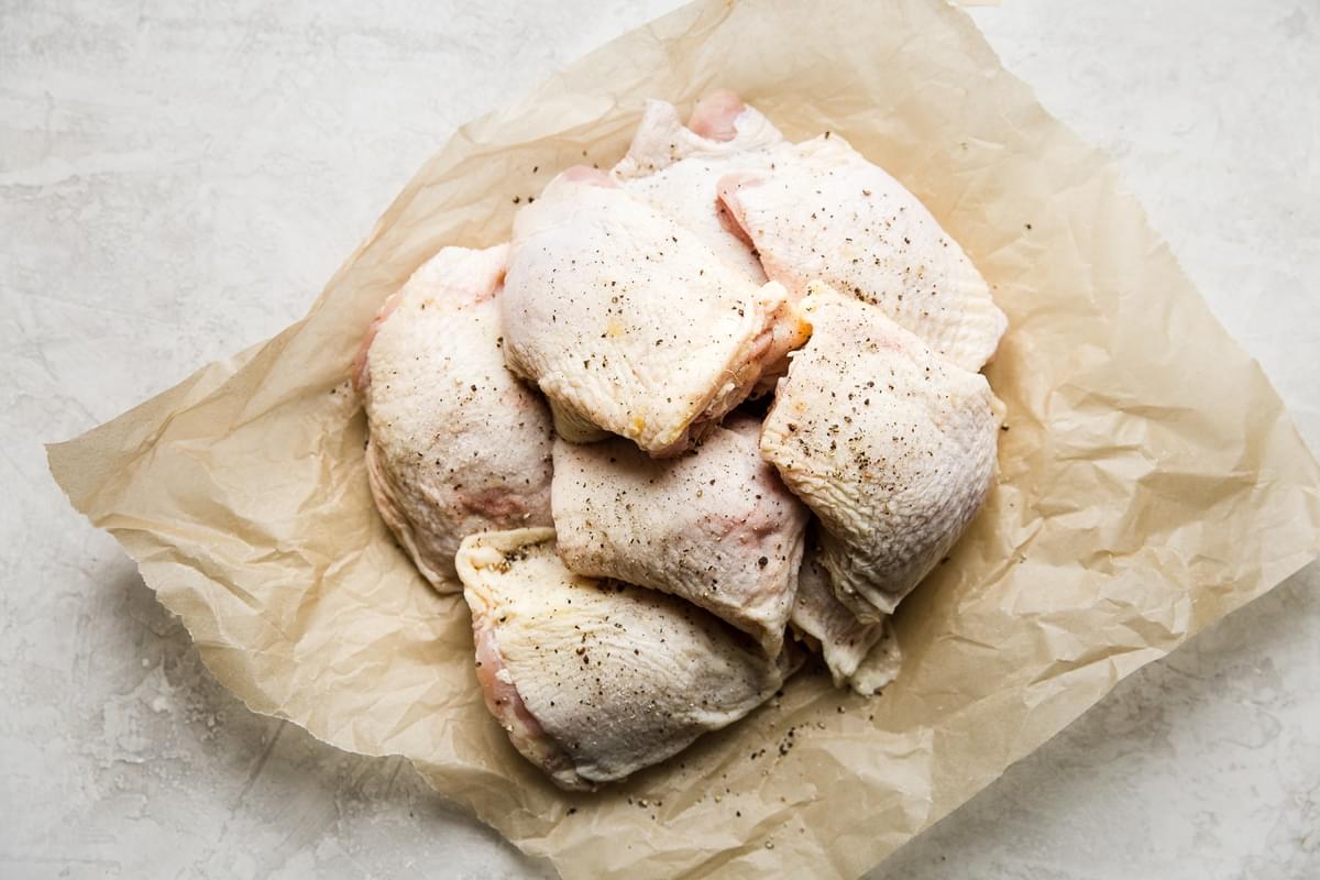 chicken thighs seasoned with salt and black pepper on parchment paper