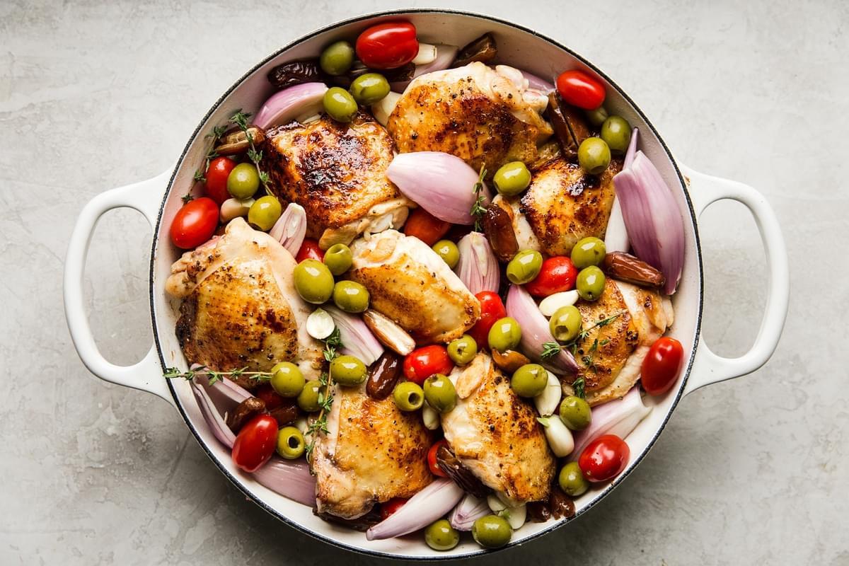 browned chicken thighs in a pan with olives, tomatoes and shallots.