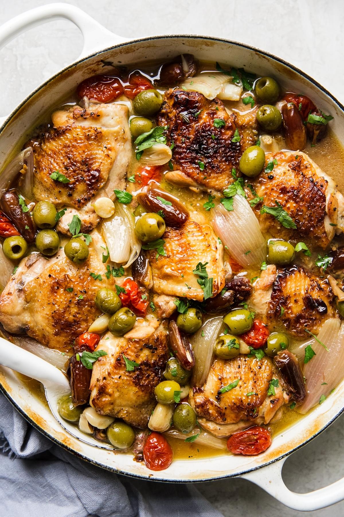 Provençal chicken with olives, tomatoes, shallots, and white wine being scooped with a serving spoon