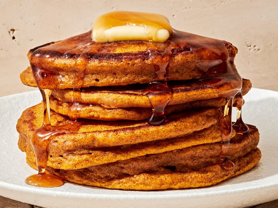 a stack of homemade pumpkin pancakes topped with a pat of butter and dripping with maple syrup