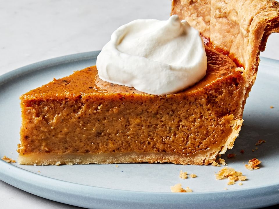 a slice of homemade pumpkin pie spiced with cinnamon, ginger, nutmeg, cloves, pepper and salt, topped with whipping cream