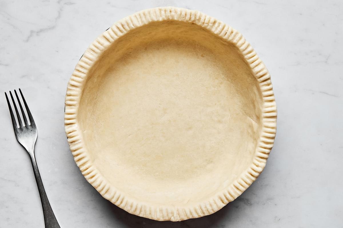 raw pie crust laid in a 9 inch deep dish pie plate with the edges trimmed and crimped with a fork