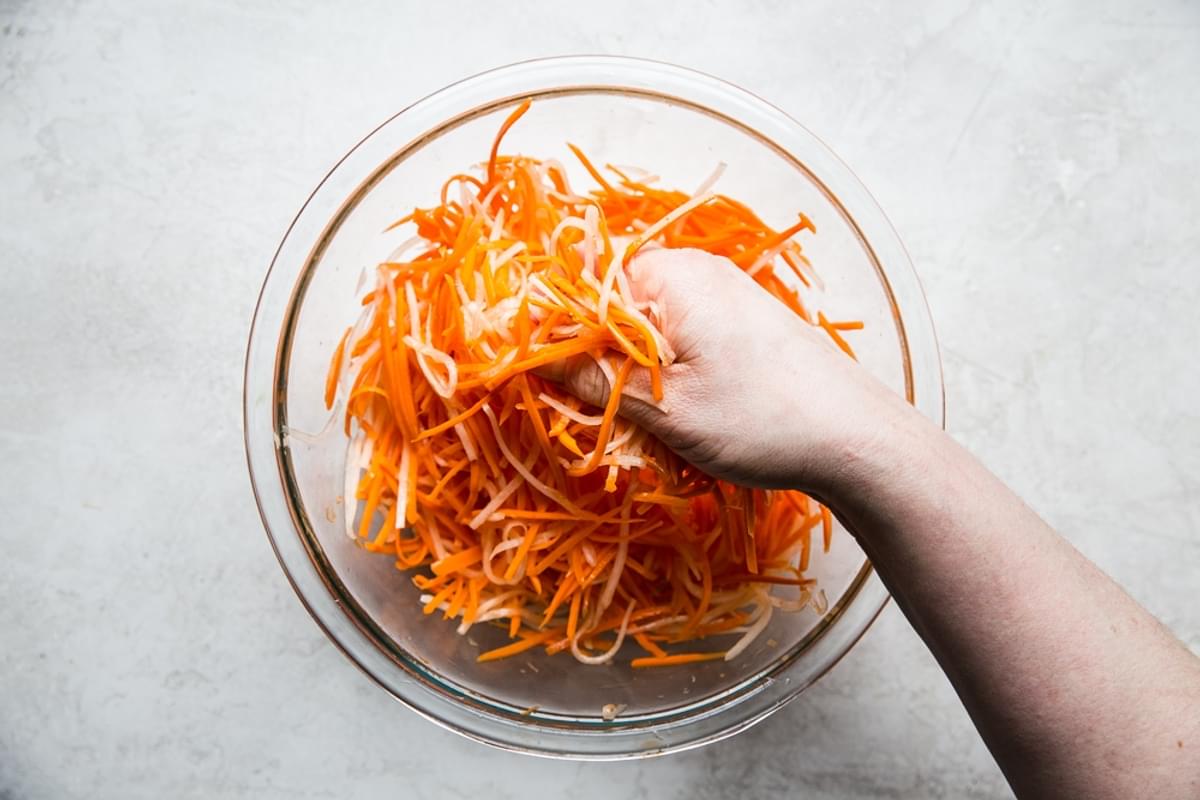 Hand mixing carrots and daikon in a bowl