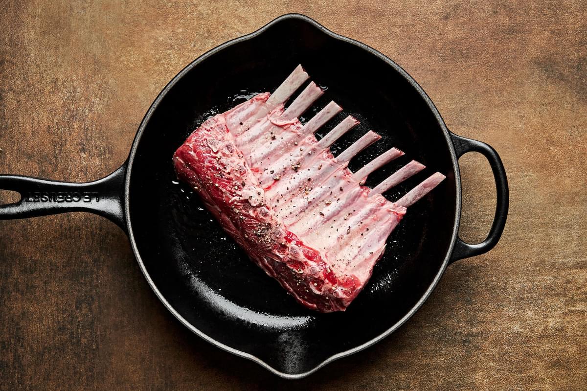 rack of lamb seasoned with salt and pepper being browned in a skillet with vegetable oil