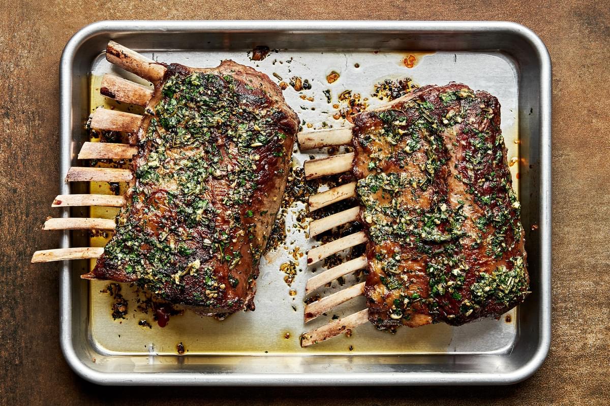 a roasted rack of lamb topped with mint sauce on a sheet pan