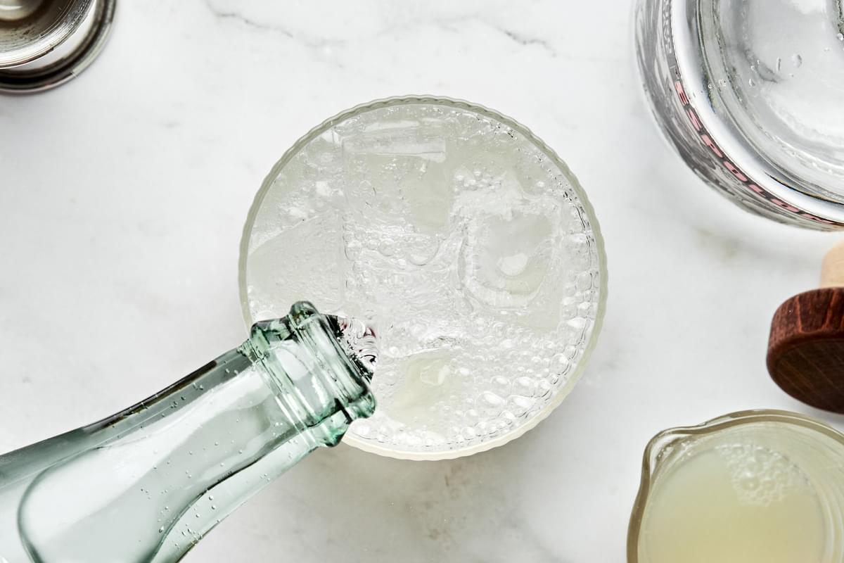 sparkling mineral water being poured into a glass with ice, tequila and lime juice