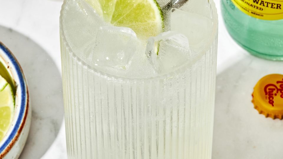 a ranch water cocktail in a glass, made with tequila, lime juice and sparkling mineral water garnished with a lime wedge