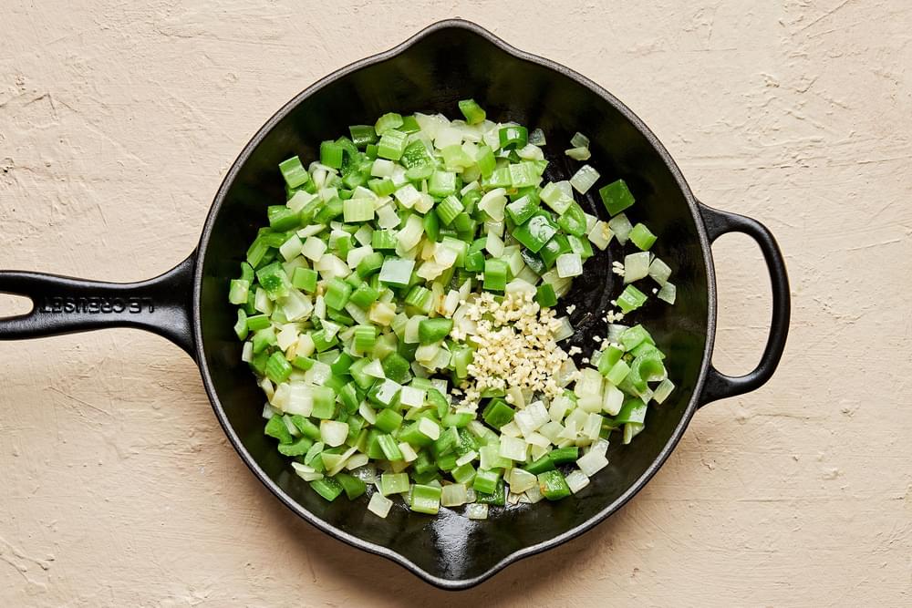 celery, onion, garlic and bell pepper being cooked in olive oil in a skillet