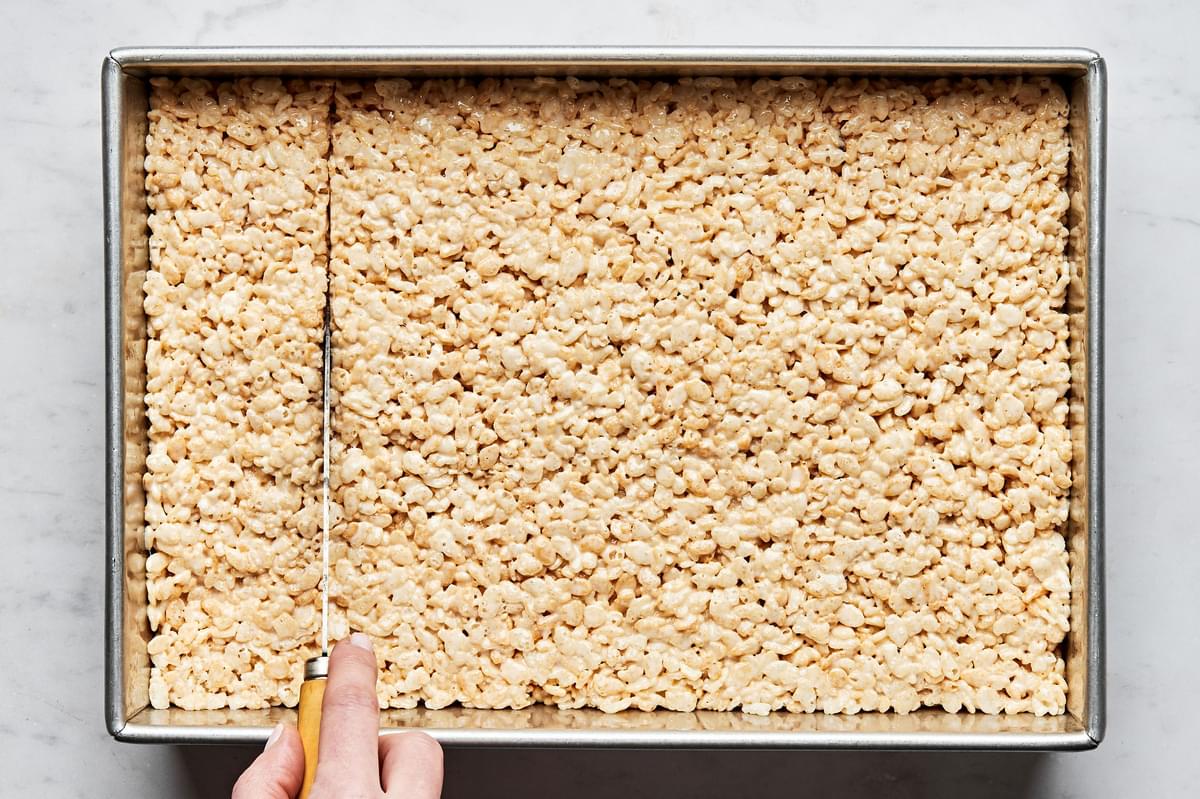 homemade rice crispy treats in a 9x13 baking pan being sliced with a knife