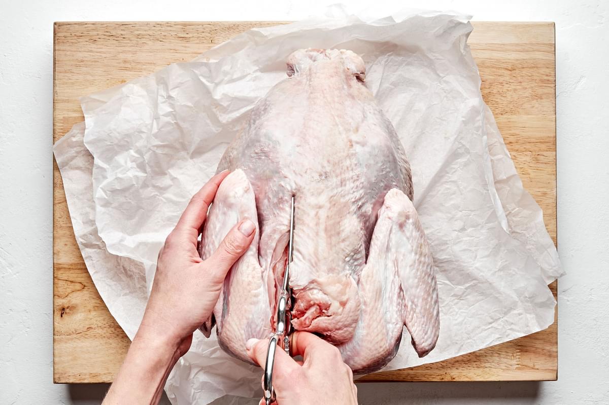 a raw turkey being spatchcocked with sharp scissors on top of parchment paper