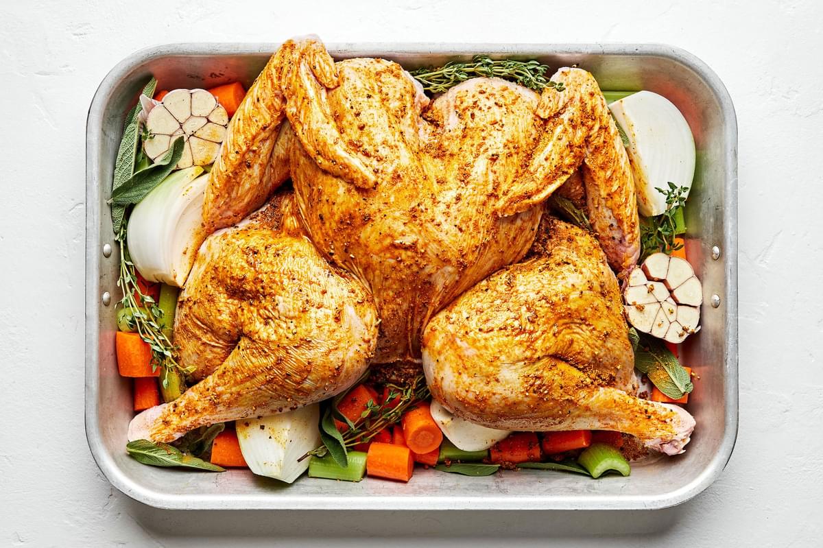 a spatchcocked turkey drizzled with olive oil and rubbed with spices on top of carrots, onion & celery in a roasting pan