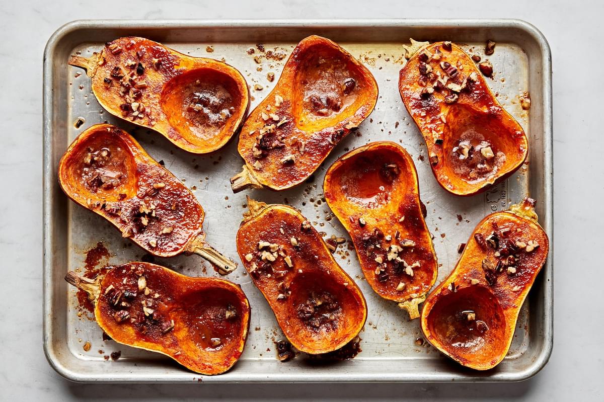 roasted honeynut squash seasoned with brown sugar, cinnamon, salt and cayenne topped with pecans on a baking sheet