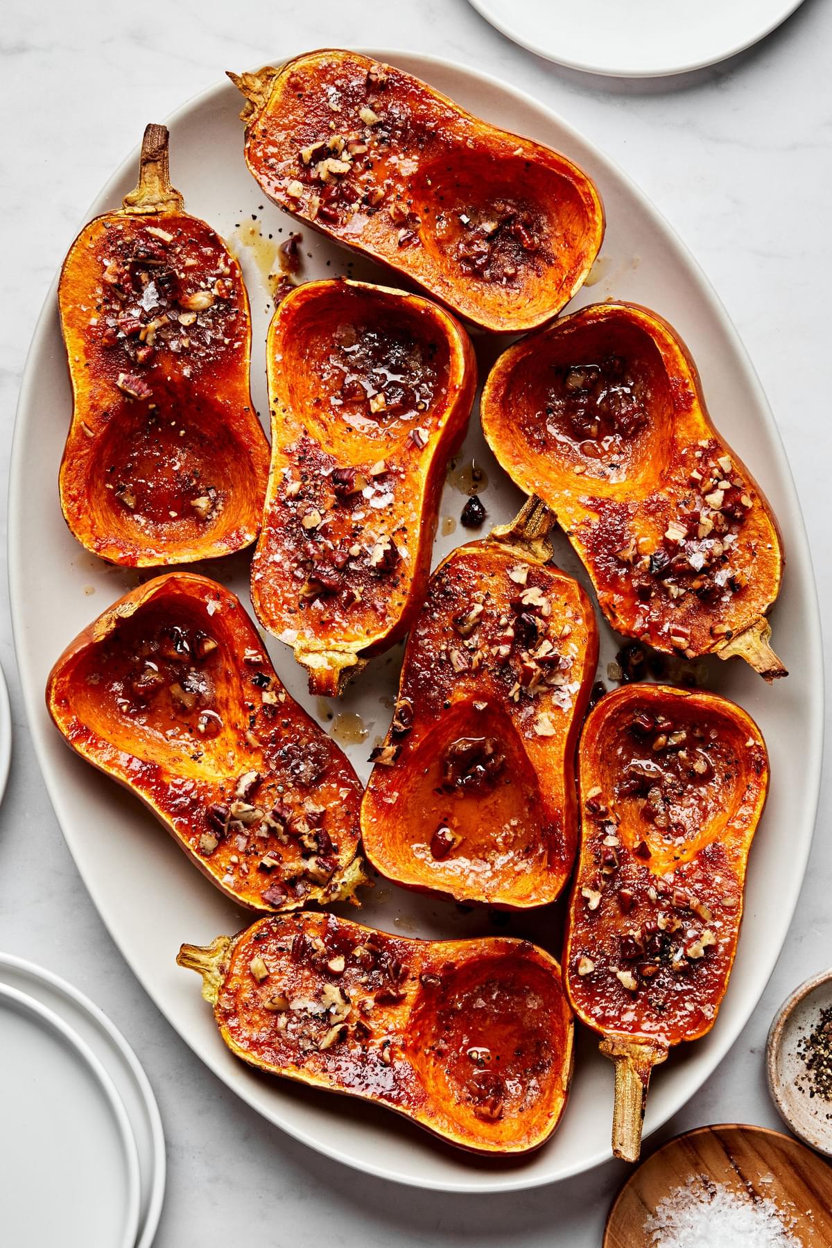 a platter of roasted honeynut squash seasoned with brown sugar, cinnamon, salt & cayenne topped with pecans on a baking sheet
