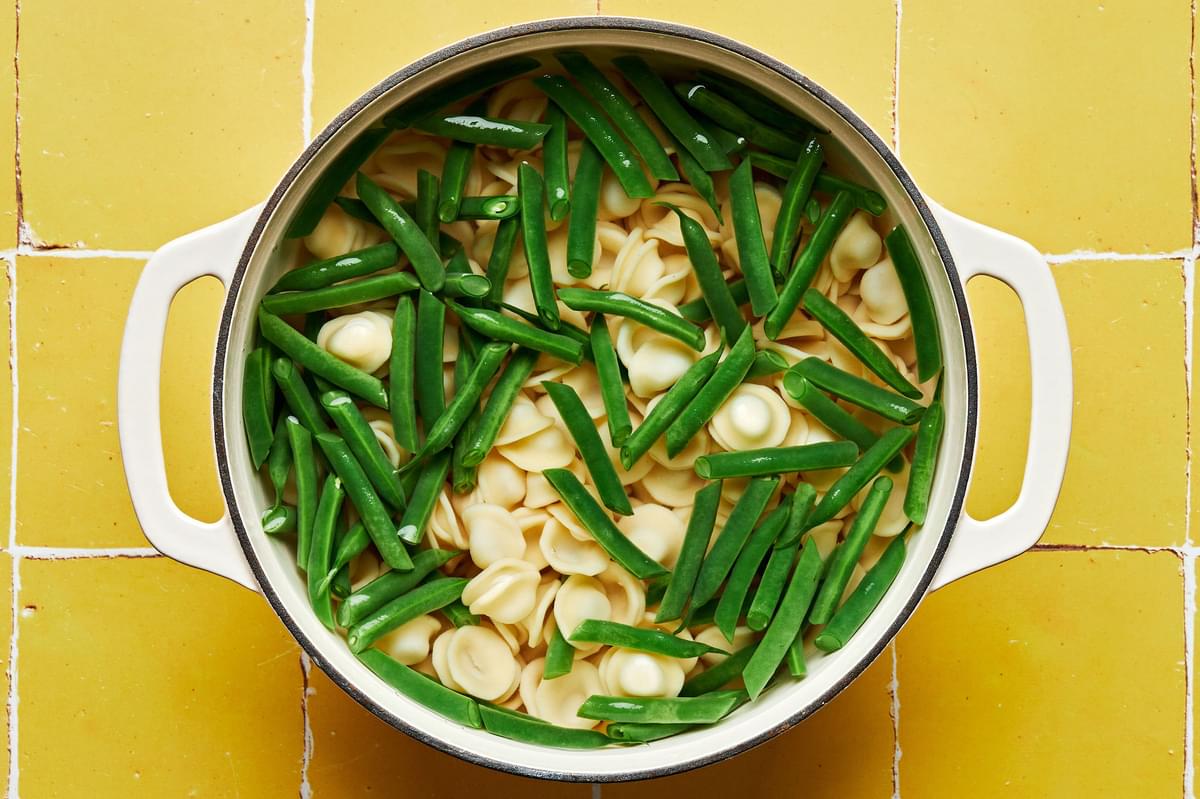 pasta and green beans being cooked in a large pot of boiling water