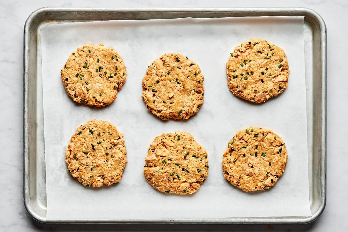 raw salmon patties on a parchment lined baking sheet made with spices,  Dijon, lemon juice, chives, mayo, egg & breadcrumbs