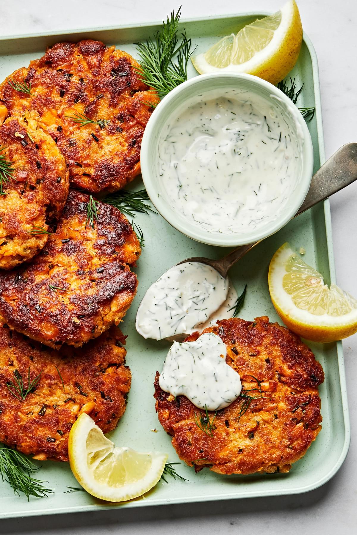 homemade salmon patties on a platter with a bowl of homemade dill dip and lemon wedges for serving