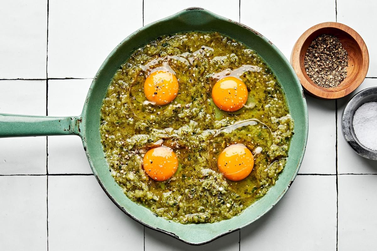 salsa verde in a skillet topped with 4 raw eggs, sprinkled with salt and pepper
