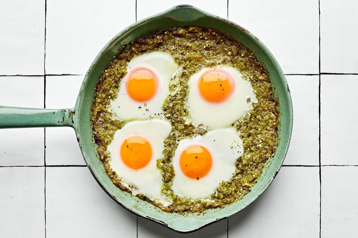 salsa verde with 4 baked eggs seasoned with salt and pepper in a skillet