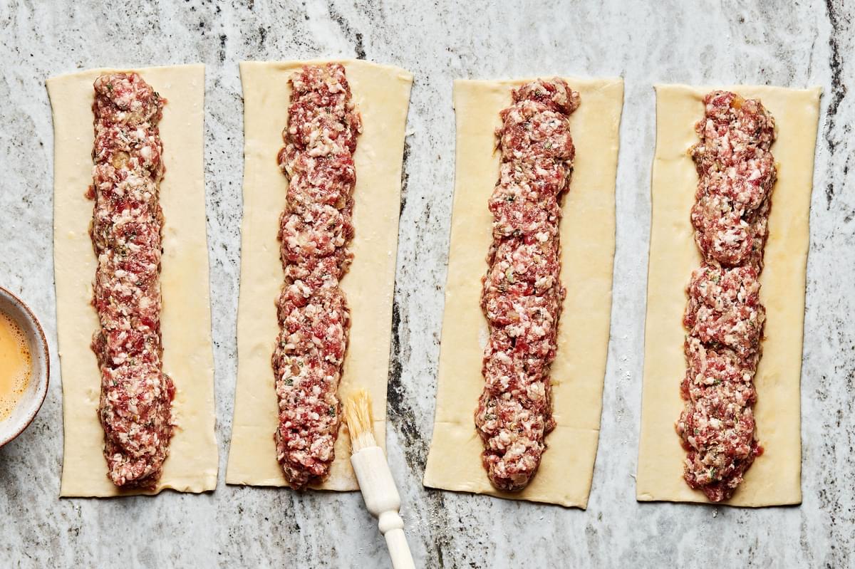 raw sausage mixture shaped in a cylinder on a rectangular piece of pastry