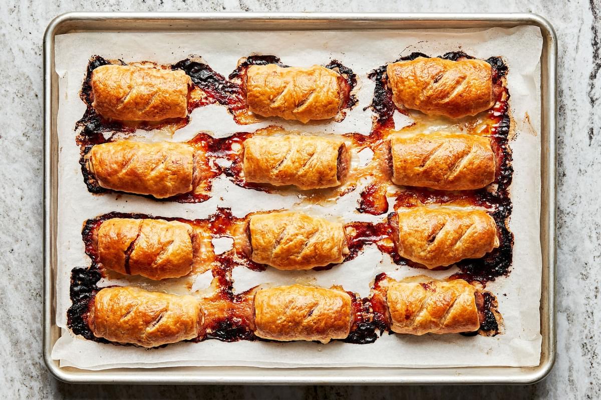 twelve sausage rolls baked on a rimed baking sheet