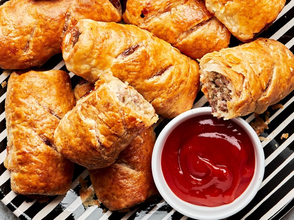 homemade sausage rolls on a black and white striped plate with a small bowl of ketchup on the plate