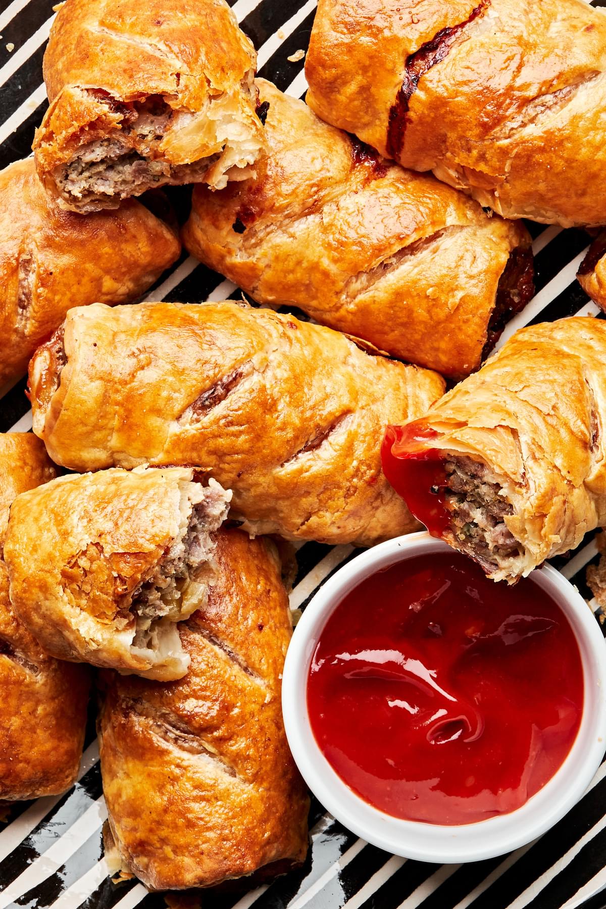 closeup of sausage rolls being dipped in a small bowl of ketchup