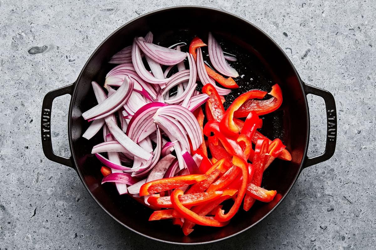 sliced bell peppers and red onion being cooked in a skillet
